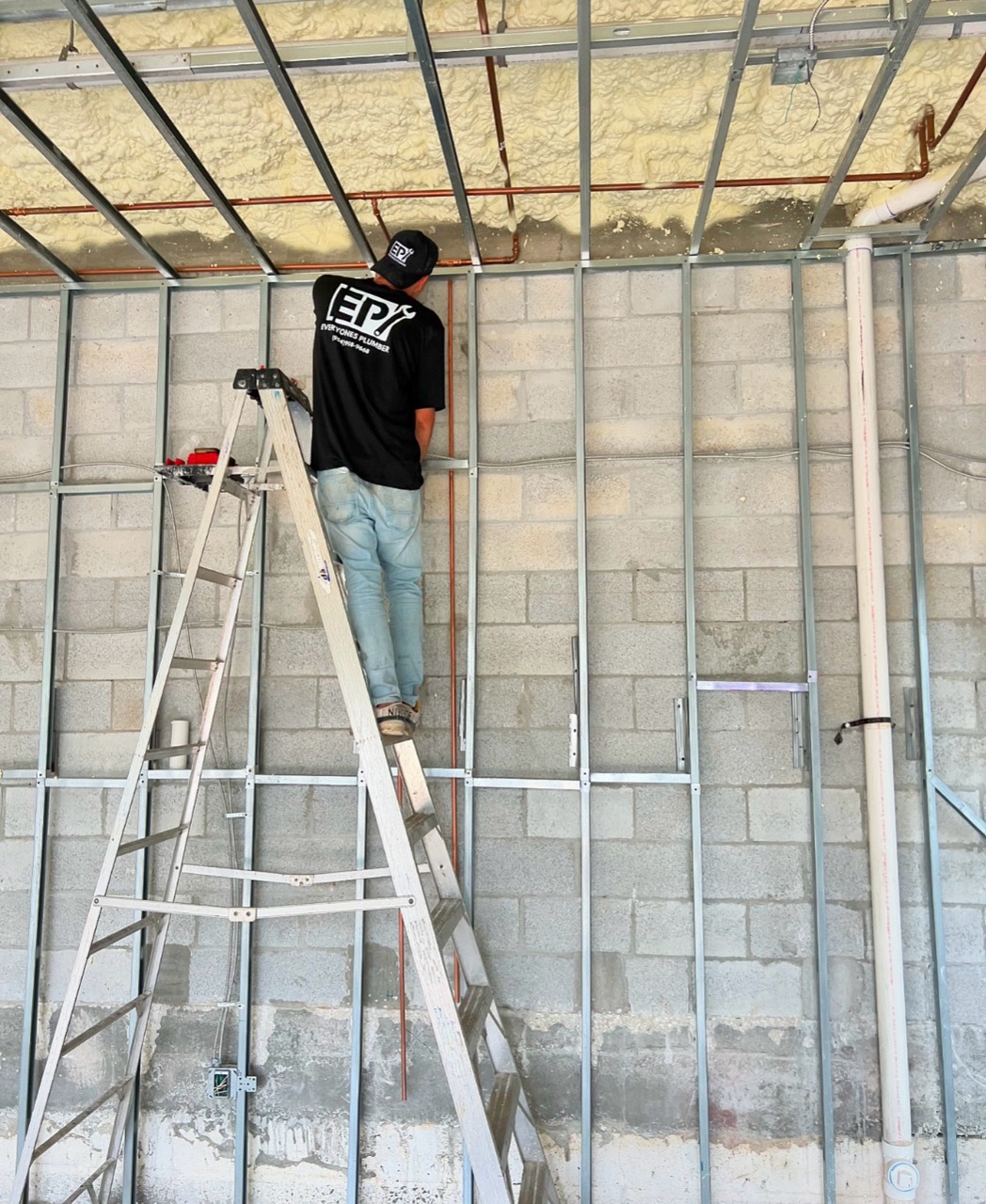 An Everyone's Plumber technician installing overhead copper pipes during construction